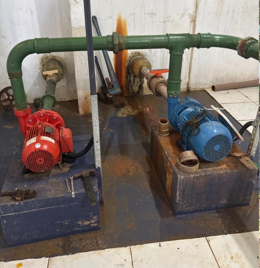 Duas bombas hidráulicas fixadas em bases de uma sala de máquinas com tubos.