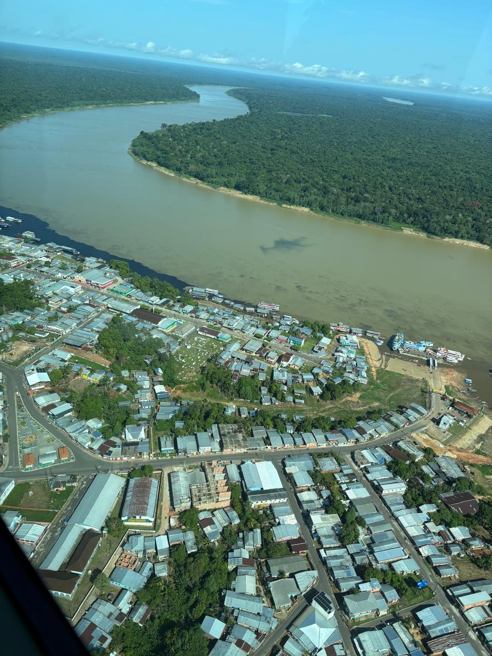 Vista aérea de uma cidade na Amazônia, ao lado de um grande rio de águas barrentas e floresta densa.