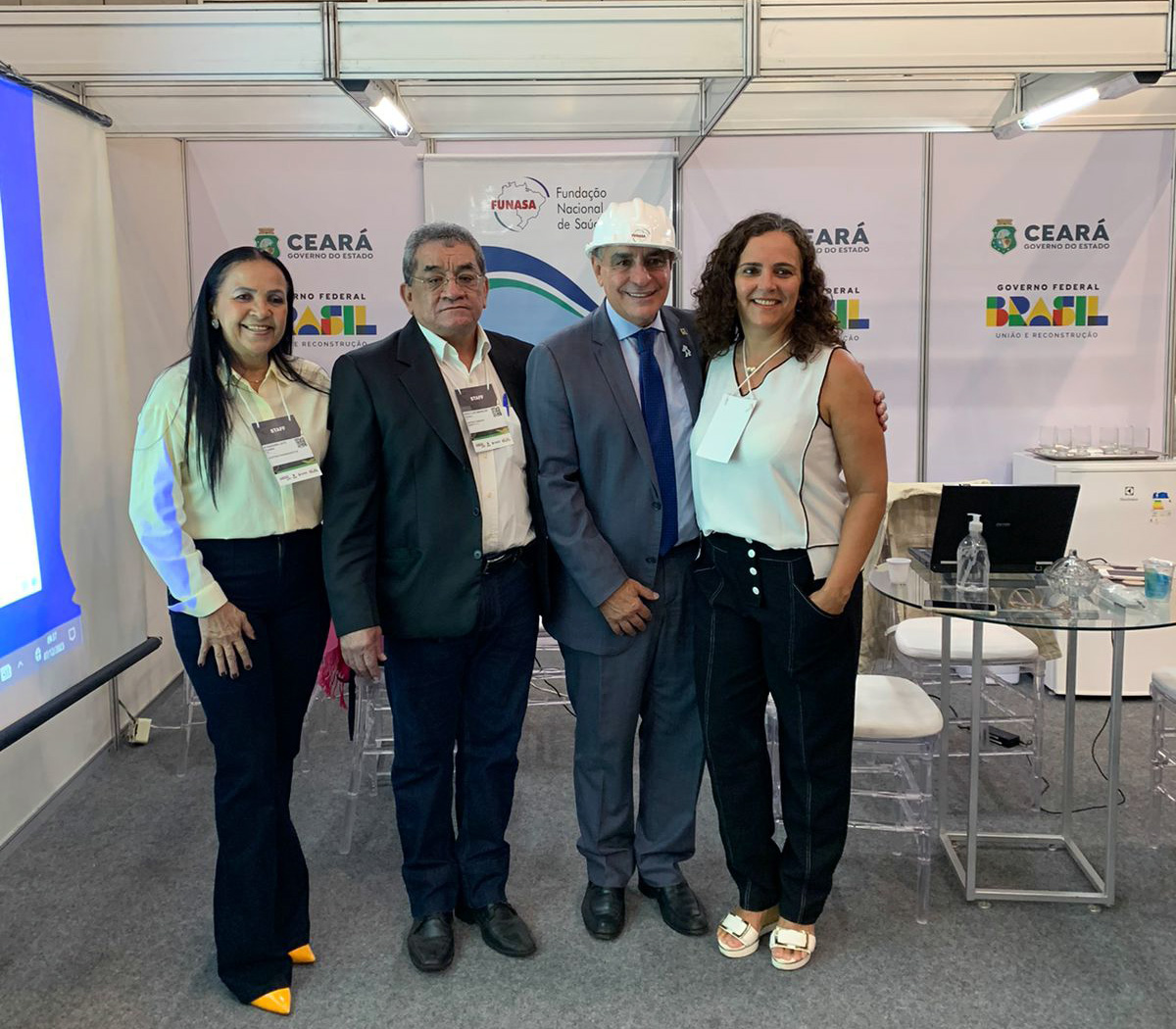 Secretário Especial de Assuntos Federativos, André Ceciliano (com capacete) é recebido no estande da Funasa pelo superintendente substituto Aureolino da Fonseca e pelas servidoras Alexandra Dias (1ª à esquerda) e Daniela Queiroz (Foto: Kaio Costa - Suest-CE/Funasa). 