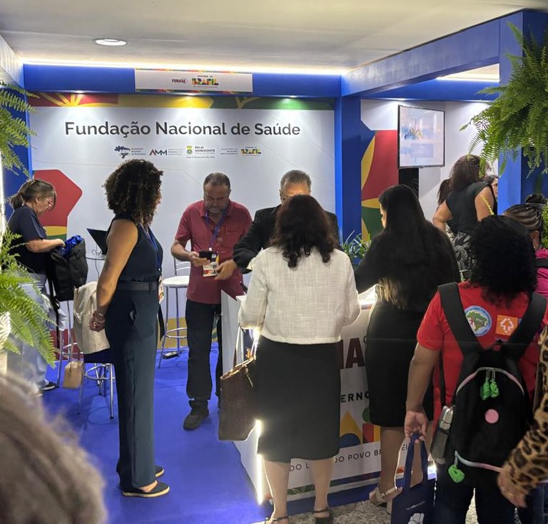 Pessoas circulam e conversam no estande da Funasa, com atendimento ativo e ambiente iluminado.