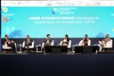 Painel com seis debatedores sentados no palco durante o Seminário Universalizar, com telão azul ao fundo exibindo o tema do evento.