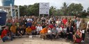 Grupo de pessoas posa ao ar livre em visita técnica, diante de estrutura de abastecimento de água, com banner institucional ao fundo e vegetação ao redor.