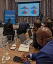Participantes assistem a apresentação com gráficos demográficos em reunião da Unicef, com notebooks e anotações sobre a mesa.