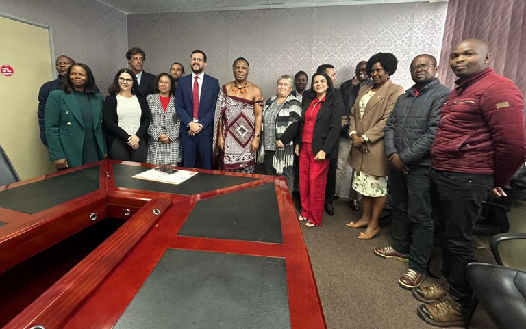 Grupo posado para foto, com pessoas vestindo trajes tradicionais coloridos e segurando lembranças em uma sala de reunião.