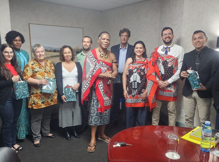 Delegação reunida para foto formal com autoridades em sala de reunião, todos alinhados em pé ao redor da mesa.