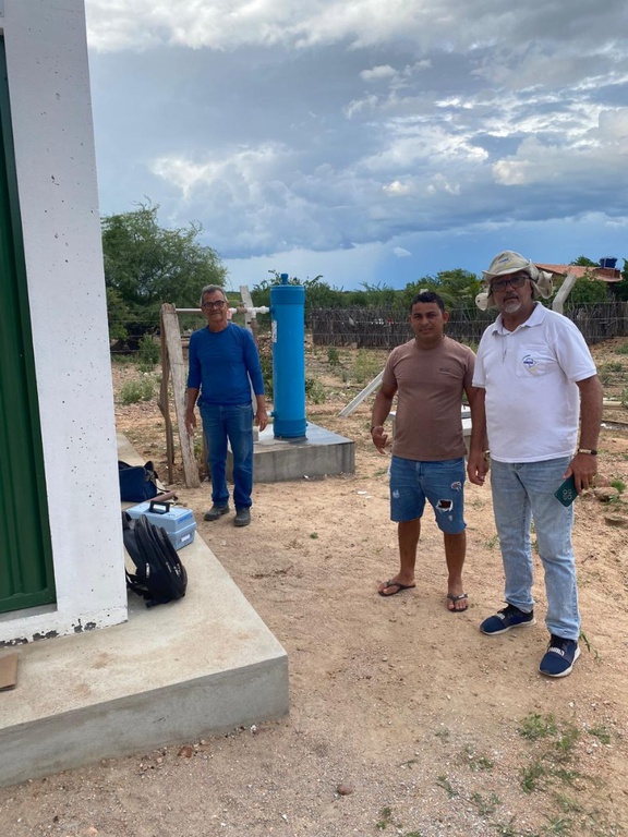 Três homens em terreno de terra ao lado de filtro de água cilíndrico azul e base de concreto da unidade Salta-Z.