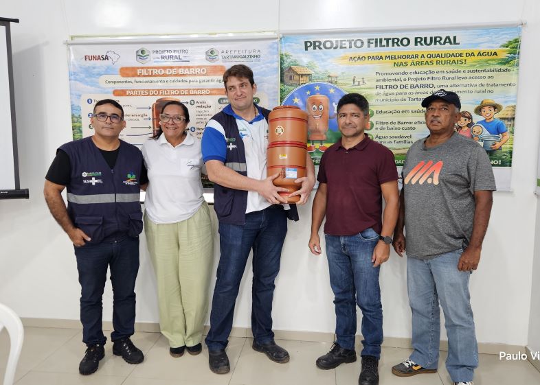 Cinco representantes da Funasa e da Prefeitura de Tartarugalzinho posam lado a lado; o homem ao centro segura um filtro de barro.