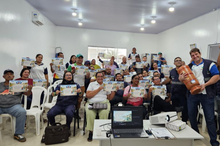 Grupo de agentes de saúde sentados e em pé em uma sala, segurando certificados e um filtro de barro ao centro.