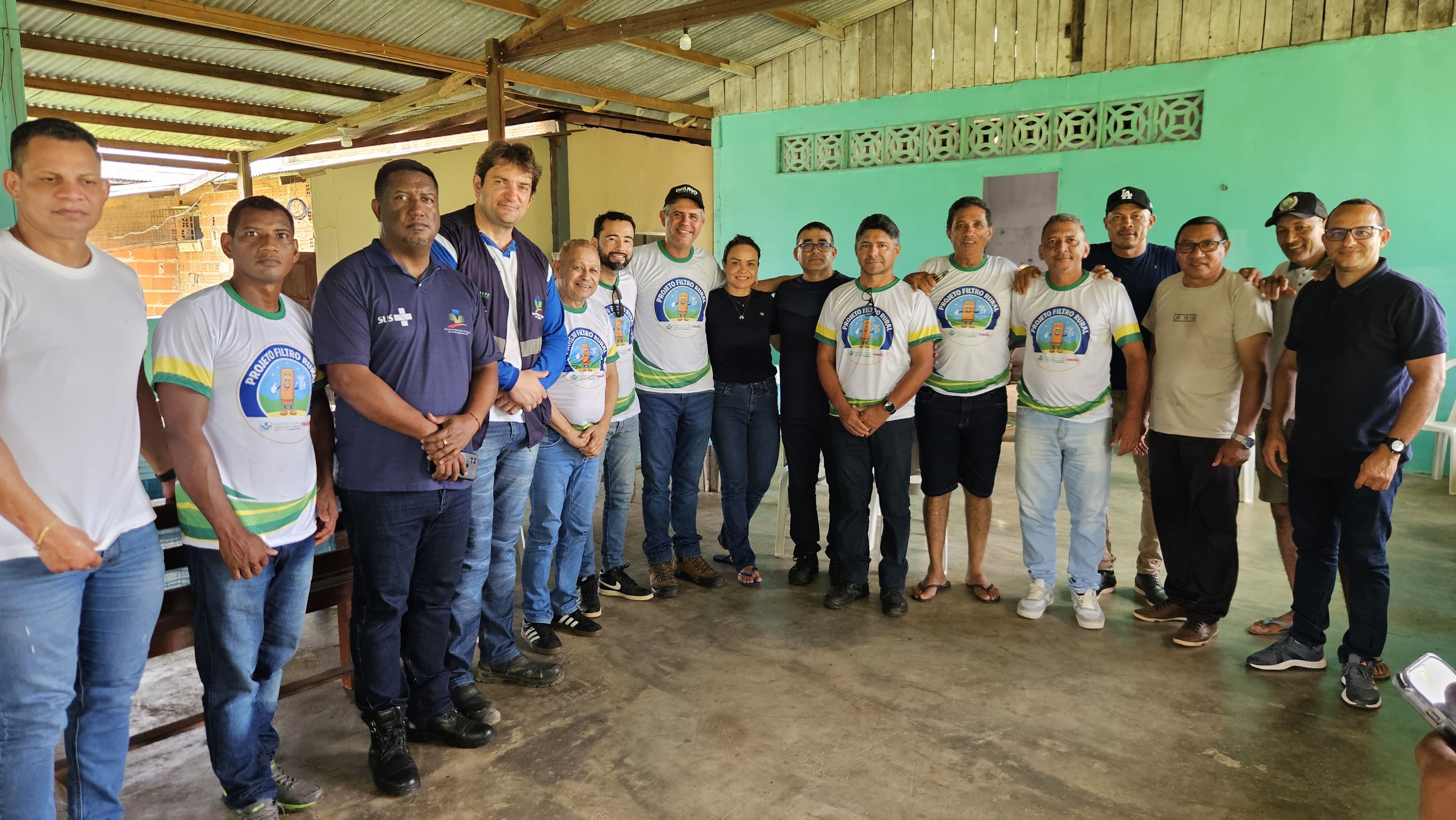 Um grande grupo de homens e uma mulher posam em pé em um salão com paredes verdes.