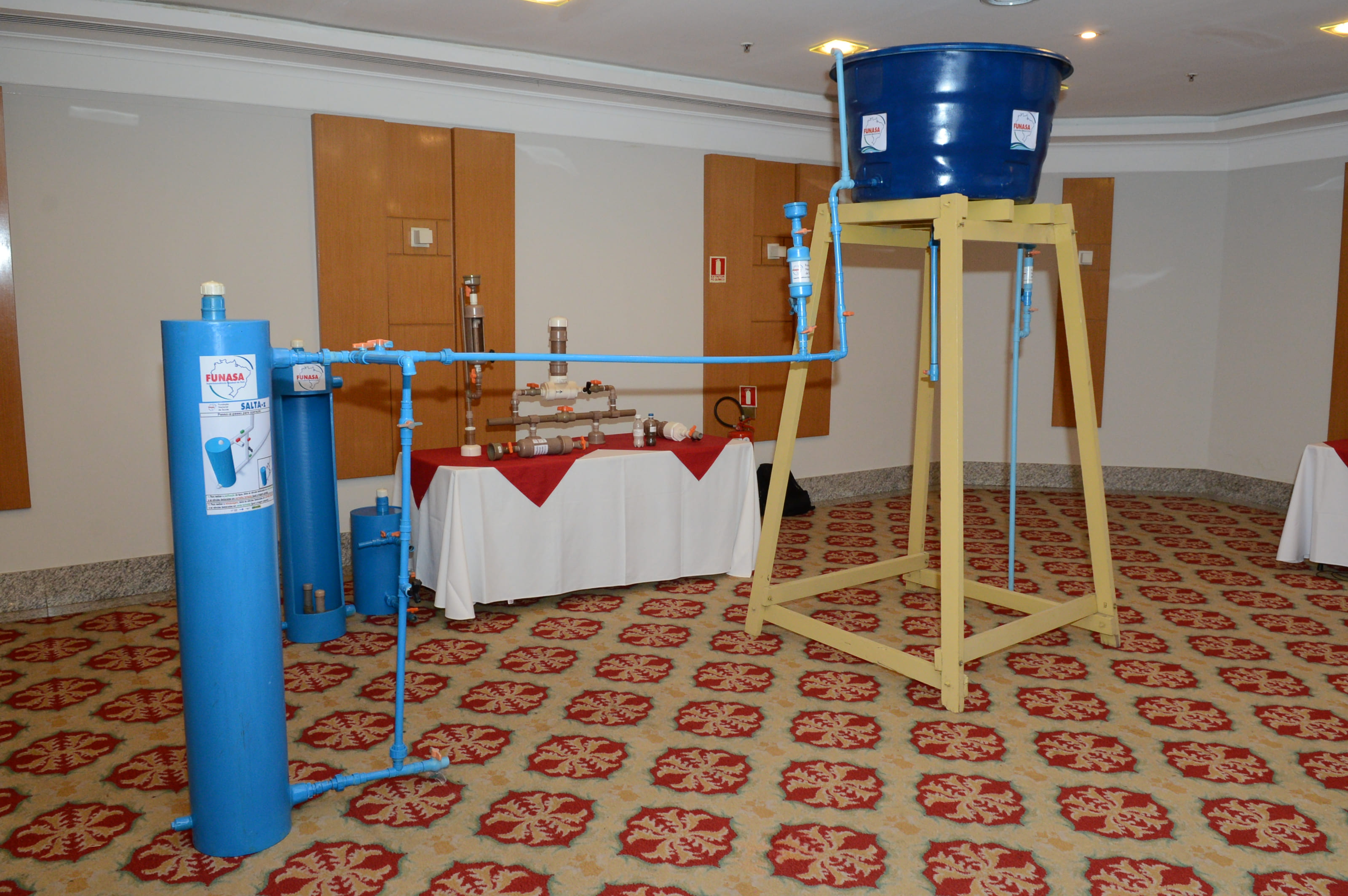 Equipamento de tratamento de água Salta-Z da Funasa montado sobre tapete decorado em salão de eventos.