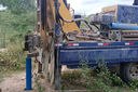 Perfuratriz montada em caminhão azul operando em solo de terra, com tubulação azul sendo inserida no poço artesiano.