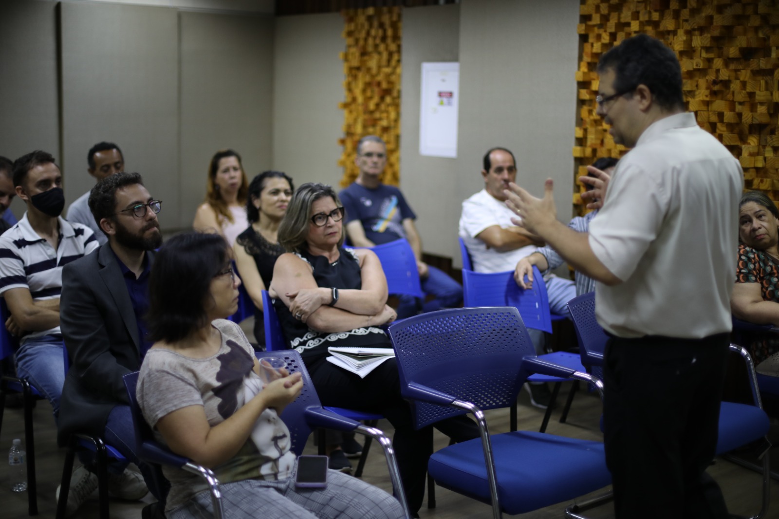 Participantes acompanham reunião técnica em auditório, atentos à explicação do palestrante sobre políticas públicas.