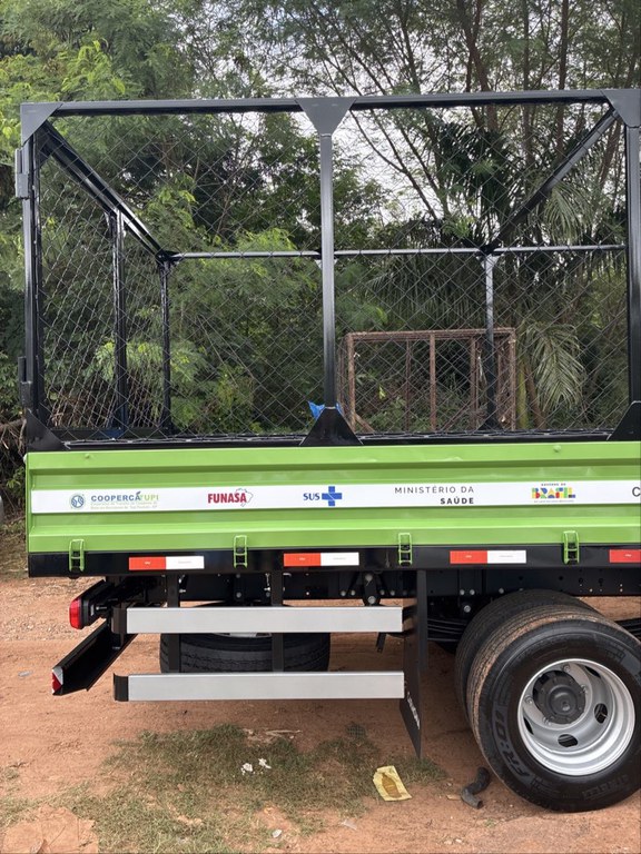 Lateral da carroceria verde com gaiola preta, logos institucionais e barra de proteção prata para ciclistas.