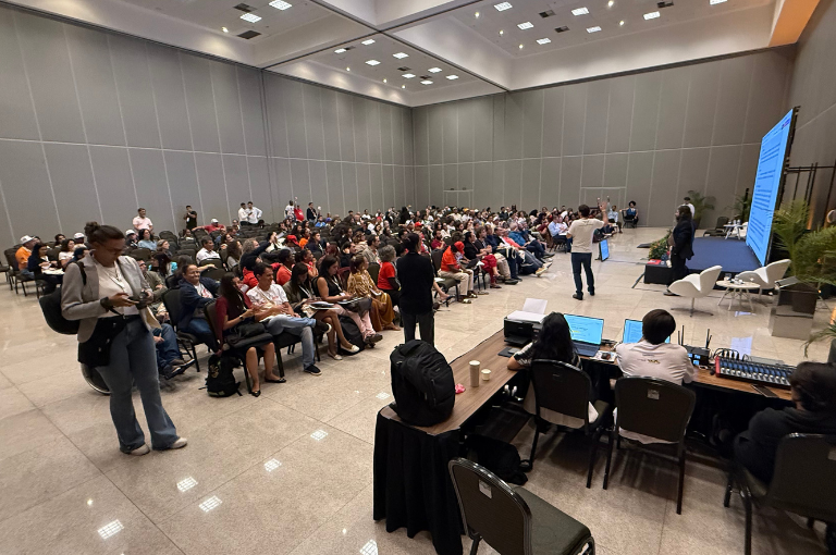 Público numeroso em auditório assiste a palestra sobre o SNDU, com palestrante em pé diante de um grande telão azul.