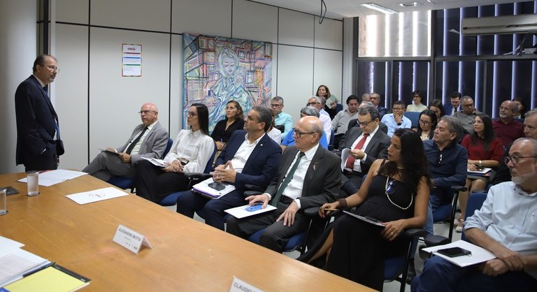 Reunião em sala institucional com dezenas de pessoas sentadas, ouvindo o presidente da Funasa em pé que faz apresentação à frente da mesa.