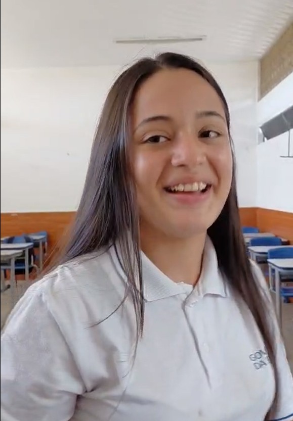 Retrato de uma jovem estudante de uniforme branco e cabelos morenos sorri para o fotógrafo.