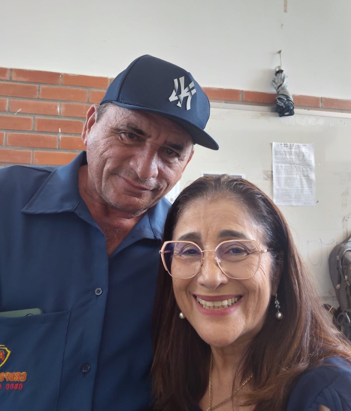 Homem de boné azul e mulher de óculos posam para foto.