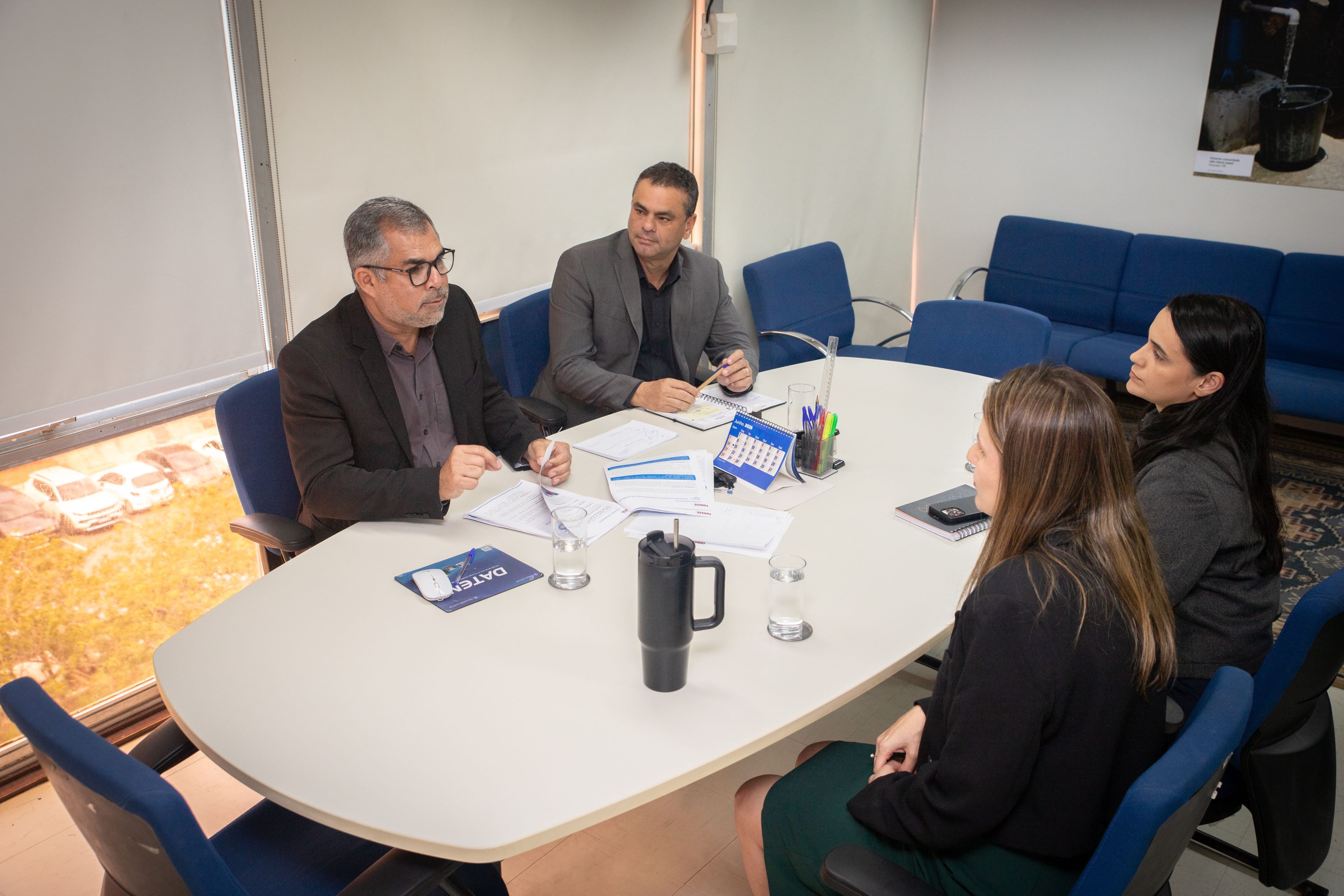 Quatro pessoas conversam reunidas em torno de uma mesa branca de escritório.