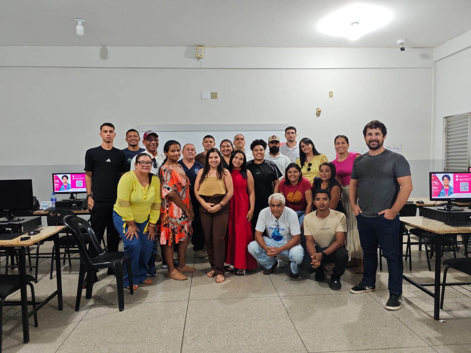 Foto oficial de um grupo numeroso de homens e mulheres sorrindo em uma sala de informática.