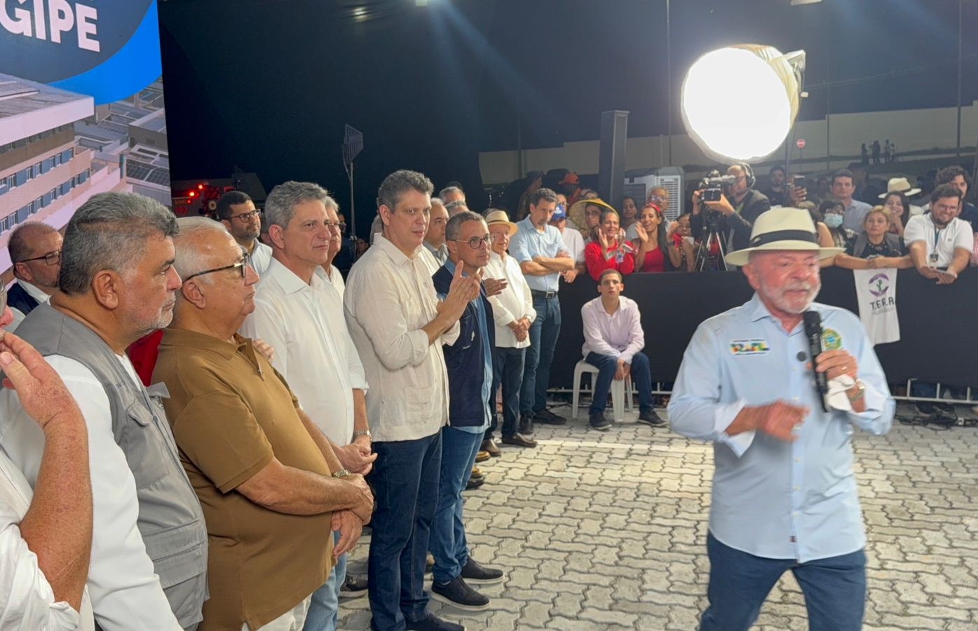 Presidente Lula fala ao microfone em evento público noturno, observado por comitiva e apoiadores em Sergipe.
