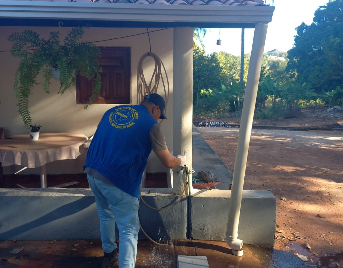 Homem de colete azul coletando água de uma torneira fora de uma casa.