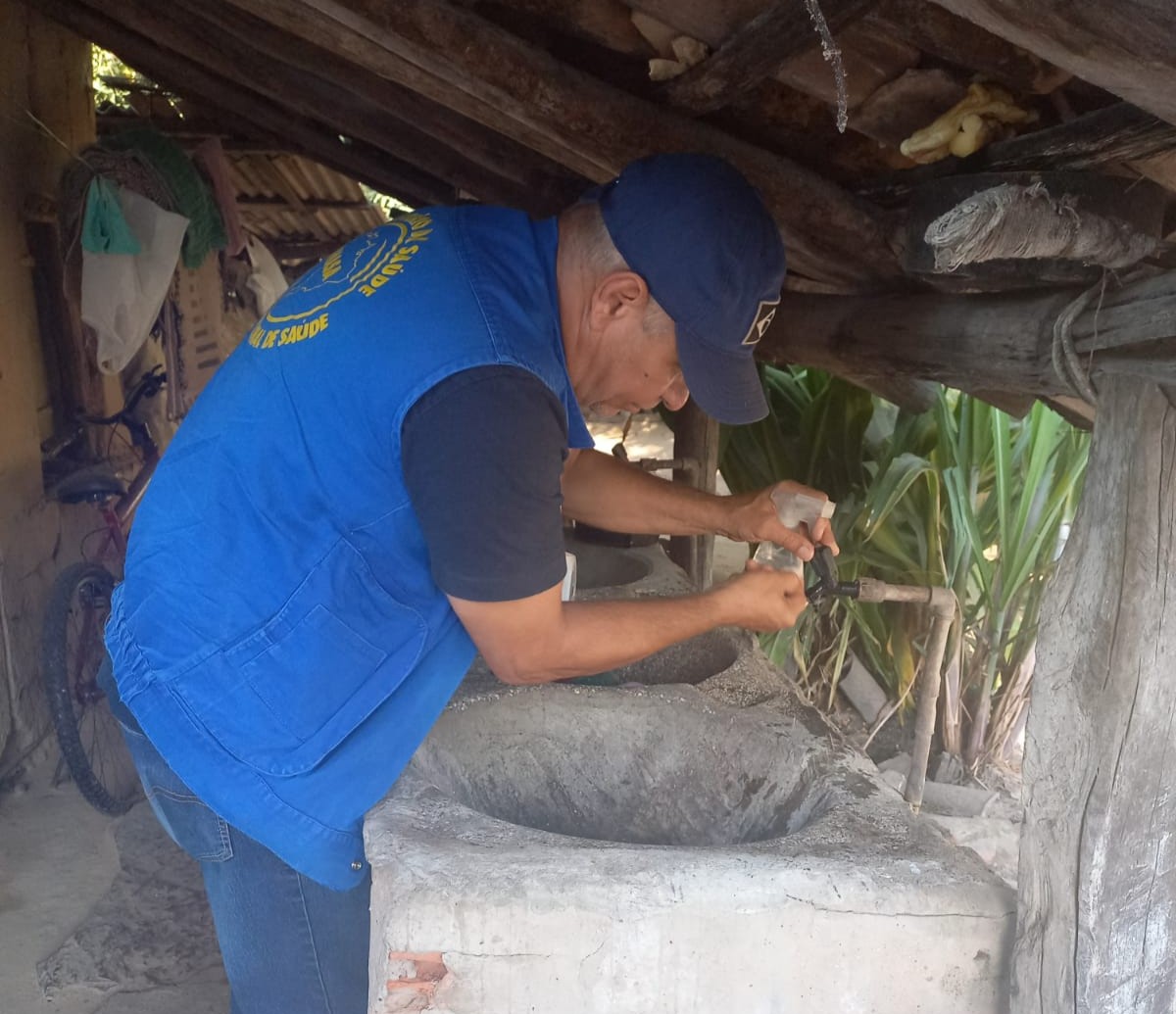 Homem de colete azul coletando agua de uma pia.