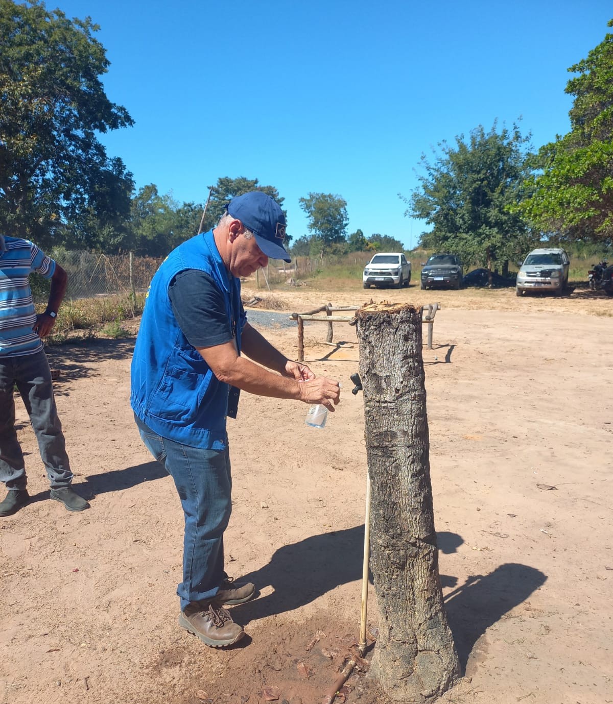 Homem coletando agua de uma torneira no meio de um campo.