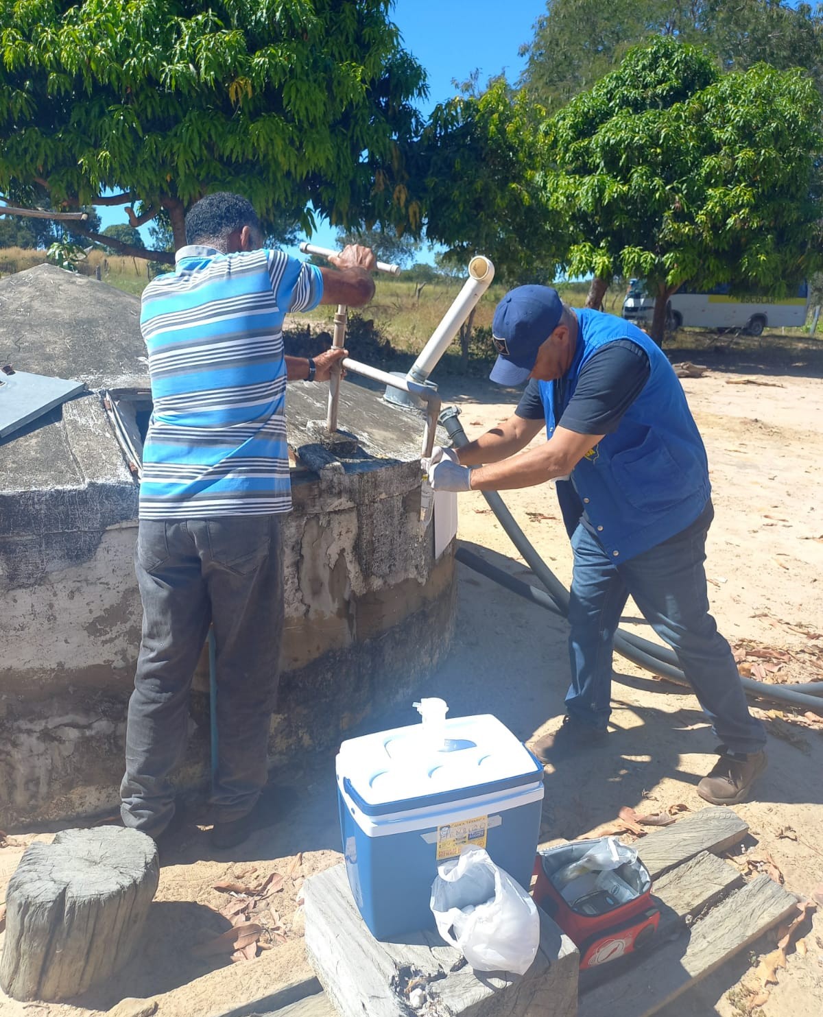 Dois homens coletando amostras de uma cisterna.