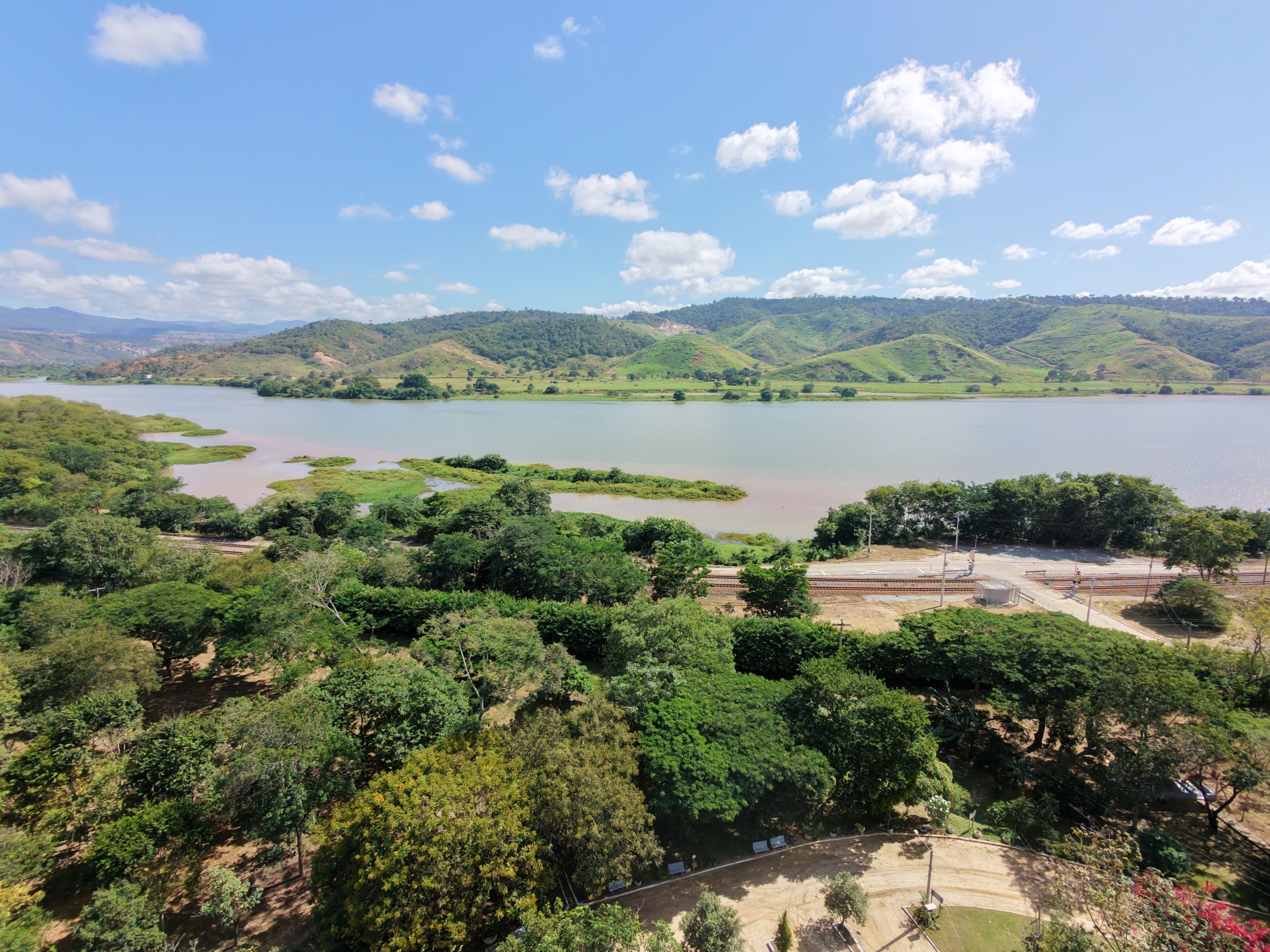 Vista aérea do Rio Doce cercado por vegetação densa, colinas verdes e céu azul ensolarado.
