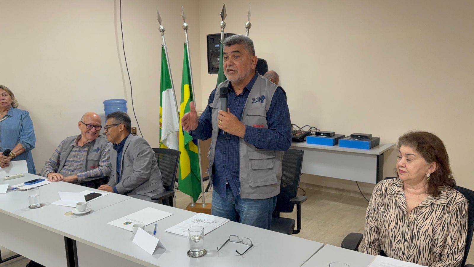 Lenildo Morais inclinado sobre mesa branca assina documento oficial com caneta azul.