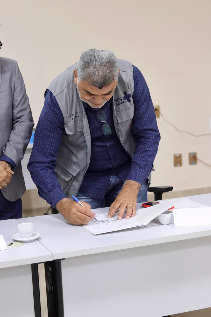 Lenildo Morais fala ao microfone em mesa com autoridades diante de bandeiras oficiais.