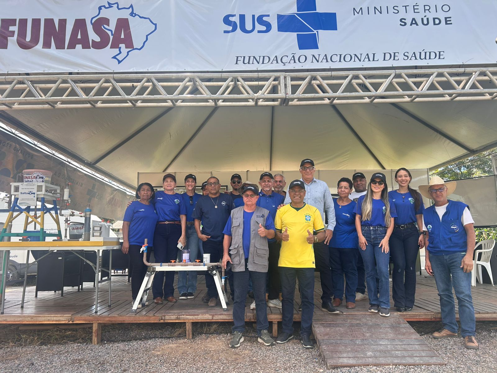 Grupo de pessoas posa reunido sob tenda com banner da Funasa e Ministério da Saúde em evento.