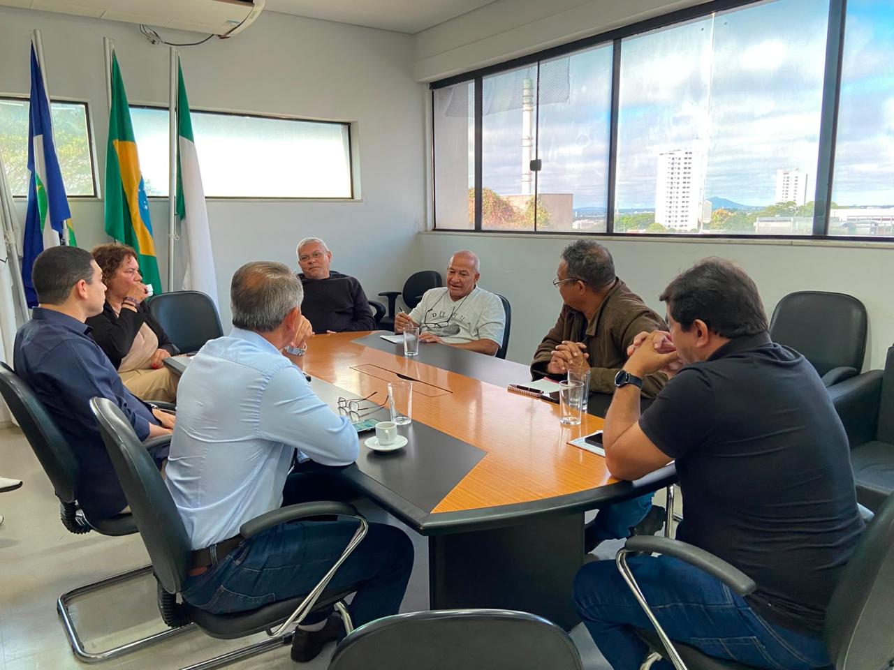 Pessoas reunidas em torno de uma grande mesa de madeira conversam em uma sala.