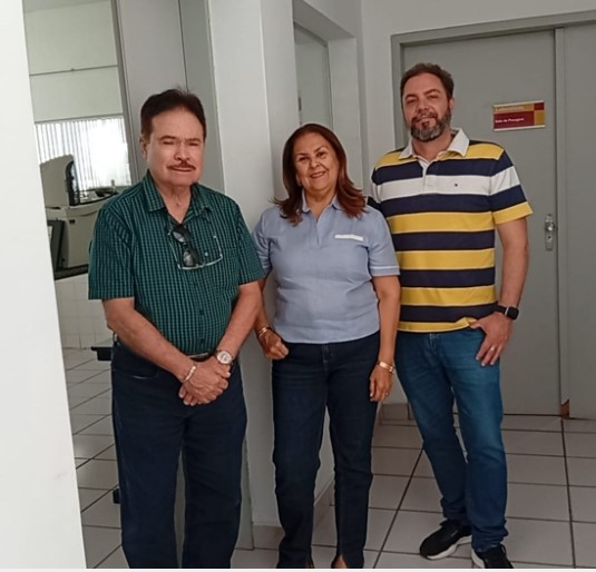 Dois homens e uma mulher posam sorrindo no corredor de entrada de um laboratório.