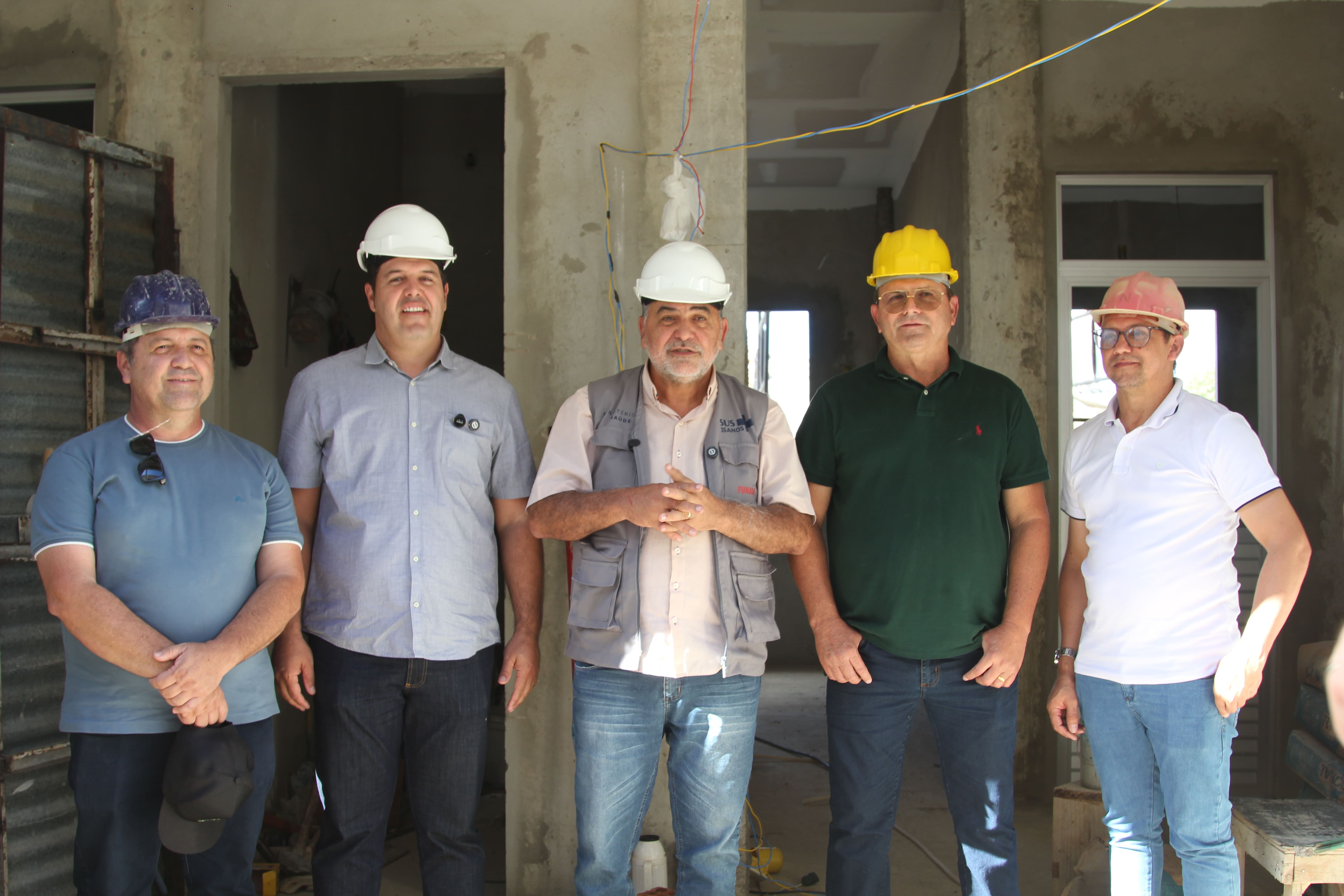 Cinco homens de capacete de proteção posam no interior de uma edificação em construção.