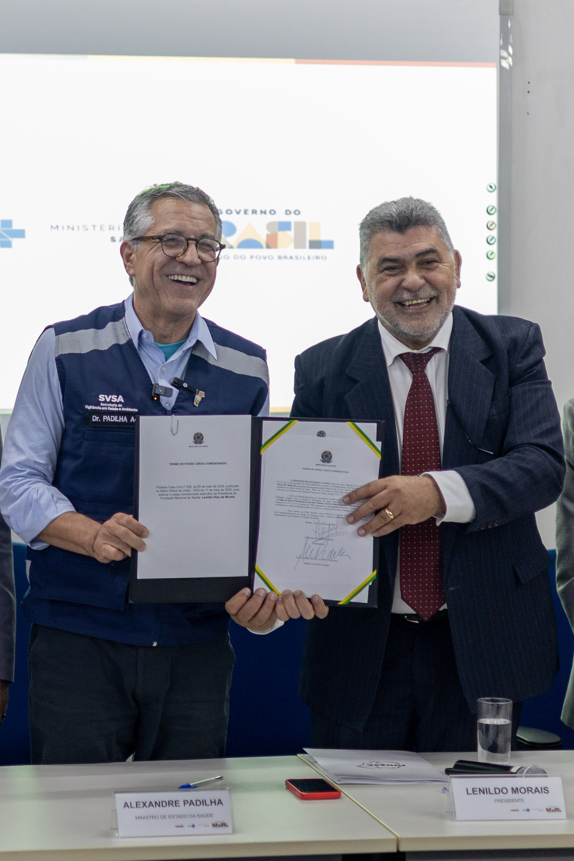 Ministro Alexandre Padilha e Lenildo Morais sorridentes, segurando juntos o termo de posse assinado.