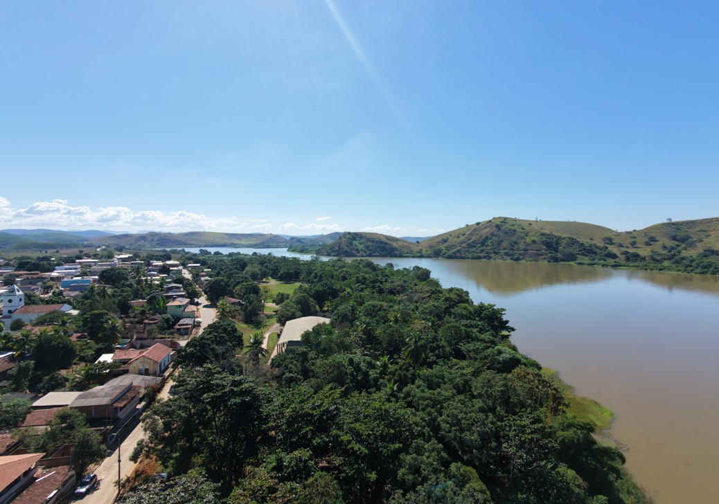 Vista aérea do Rio Doce margeando uma pequena cidade, com vegetação densa e colinas ao fundo.