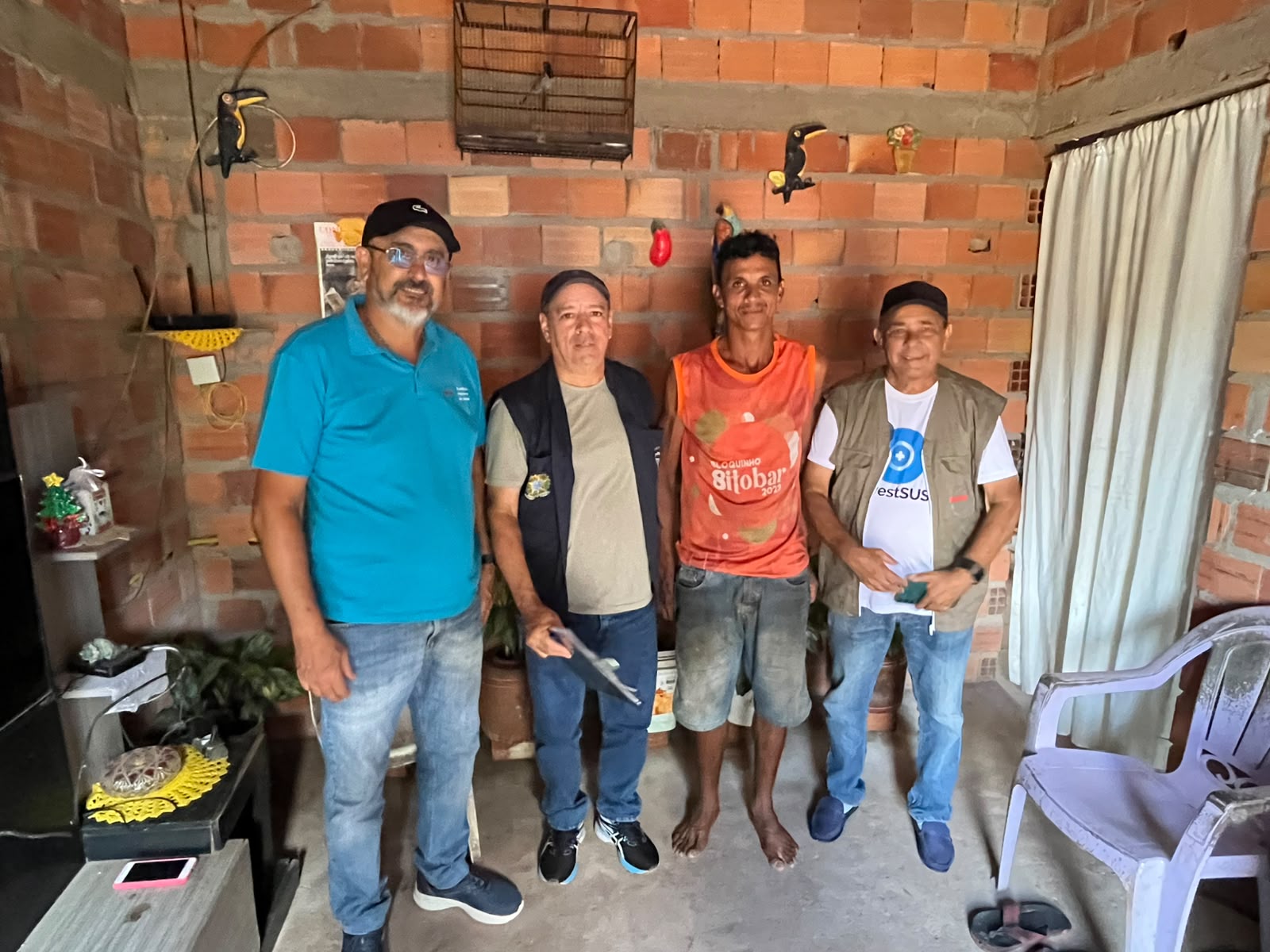 Quatro homens posando para foto em casa de aparência rústica.