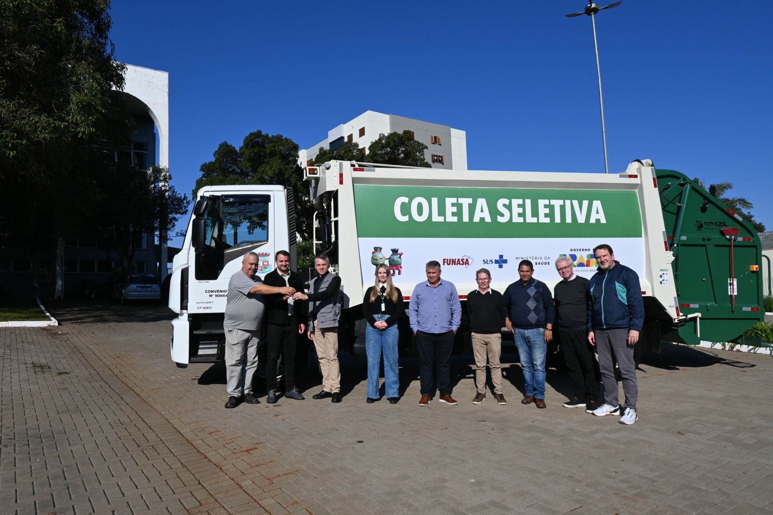 Grupo de nove pessoas posa para foto ao lado de um caminhão branco de coleta seletiva.