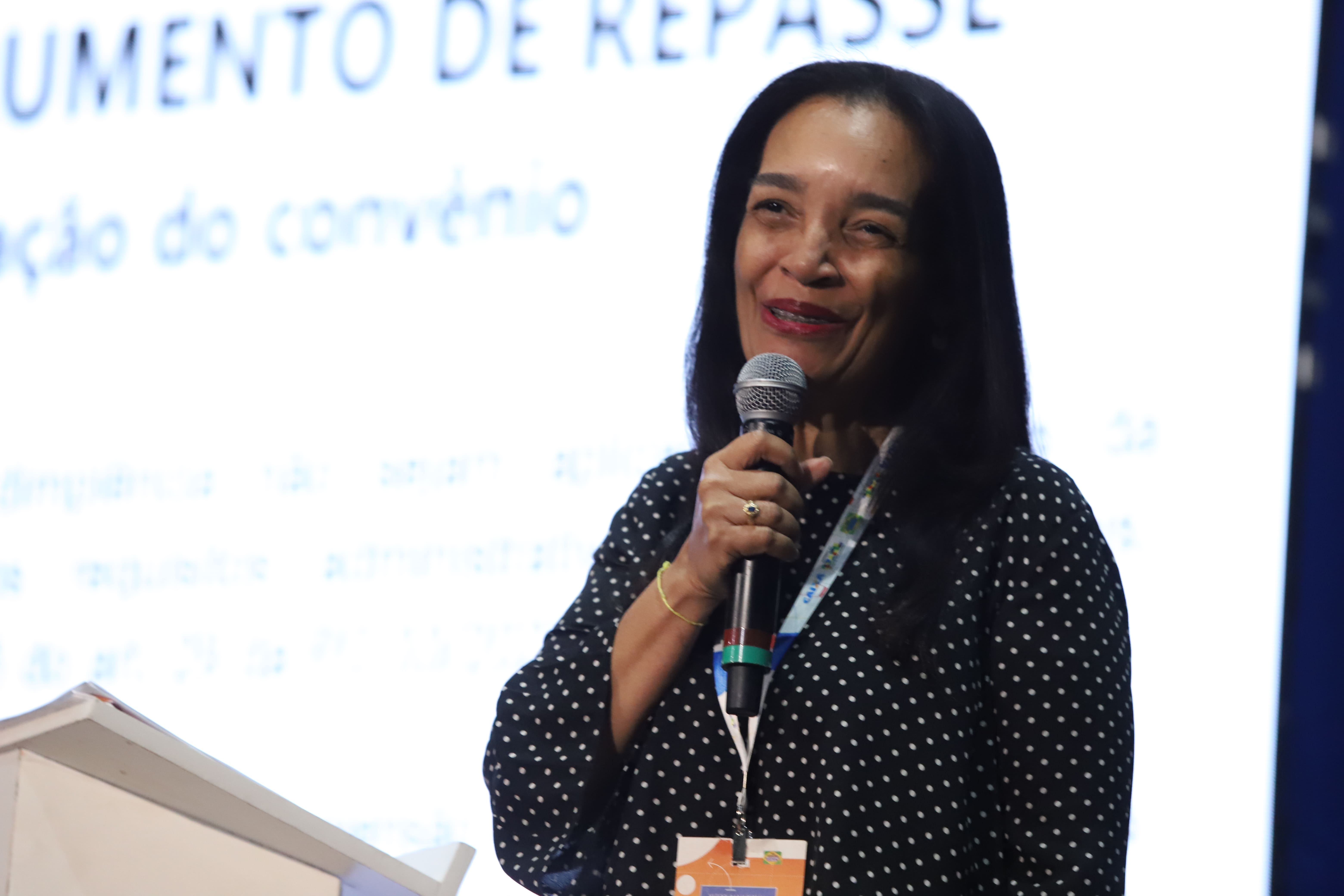 Mulher com microfone na mão e sorrindo.