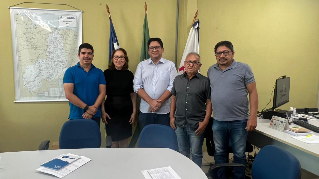 Cinco pessoas posam lado a lado em um escritório com bandeiras e um mapa ao fundo.