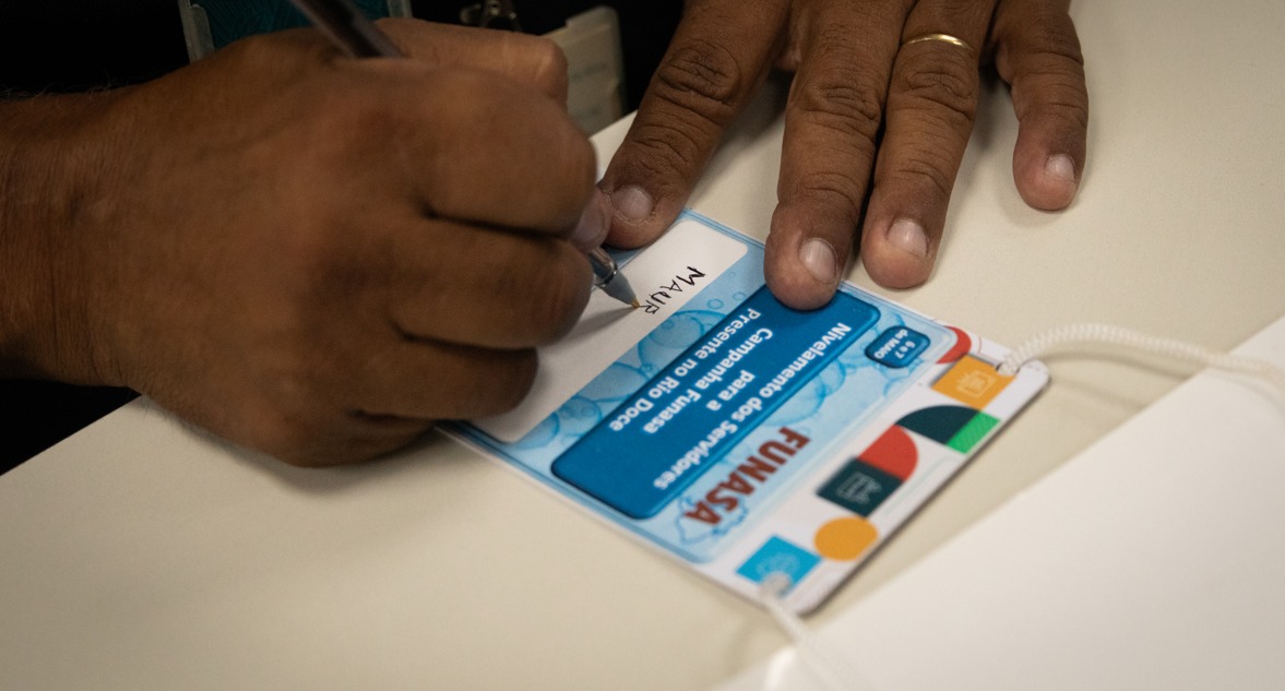 Mão de técnico escrevendo nome em crachá da campanha Funasa Presente no Rio Doce.