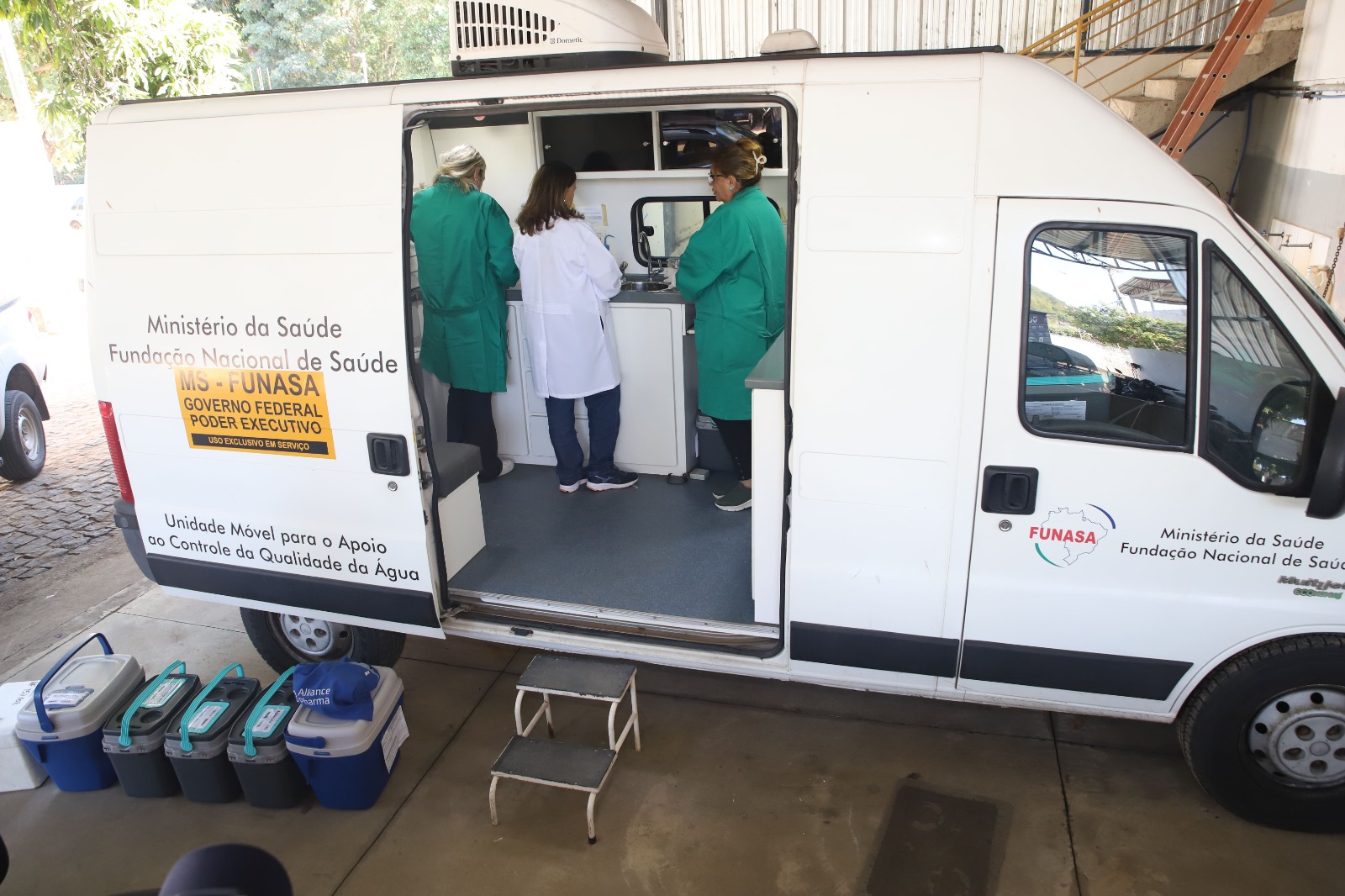 Profissionais com jaleco trabalham no interior de uma unidade móvel de análise de água.