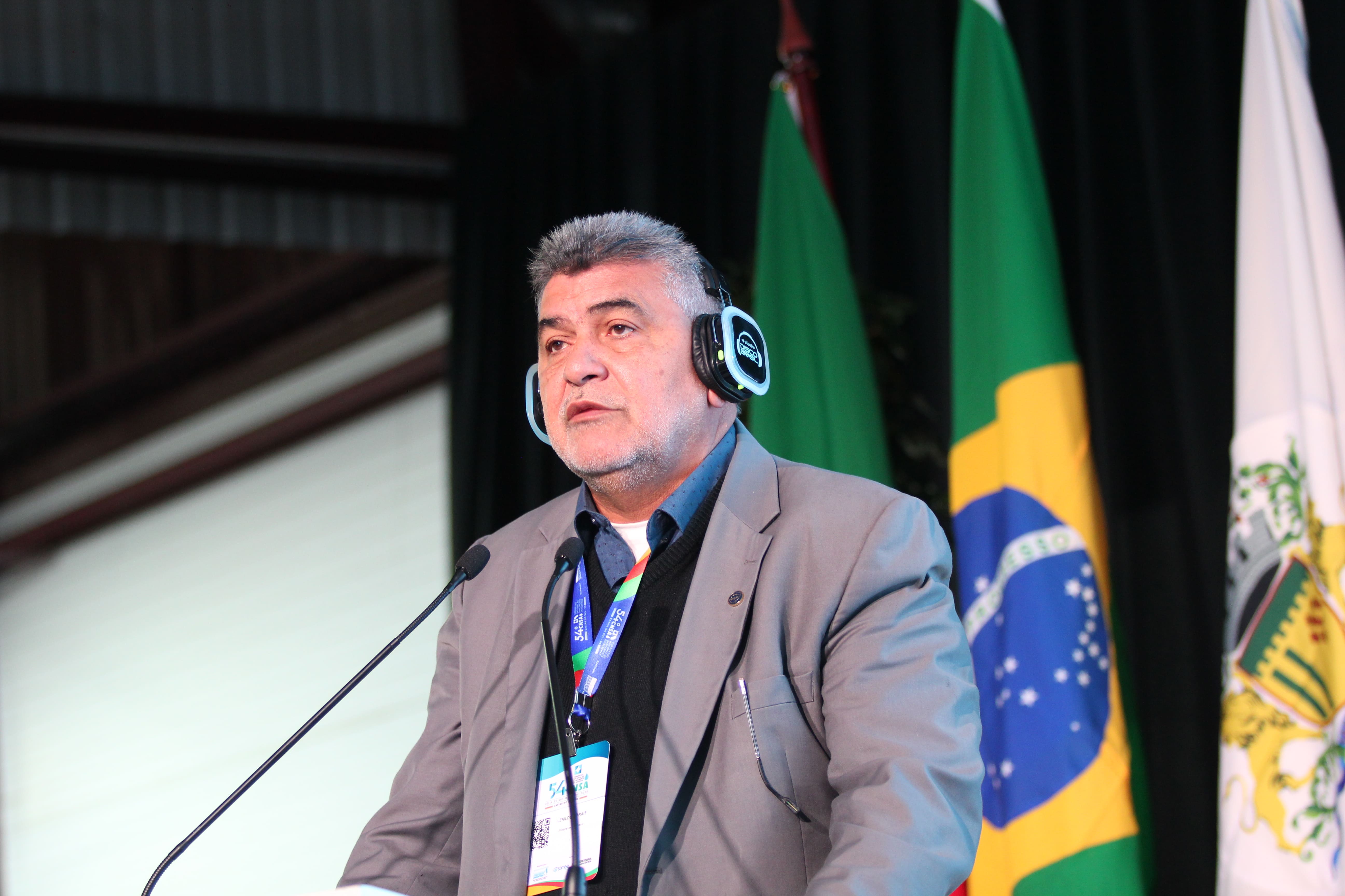 Presidente da Funasa, Lenildo Morais, em plano médio, discursa com fones de ouvido no evento.