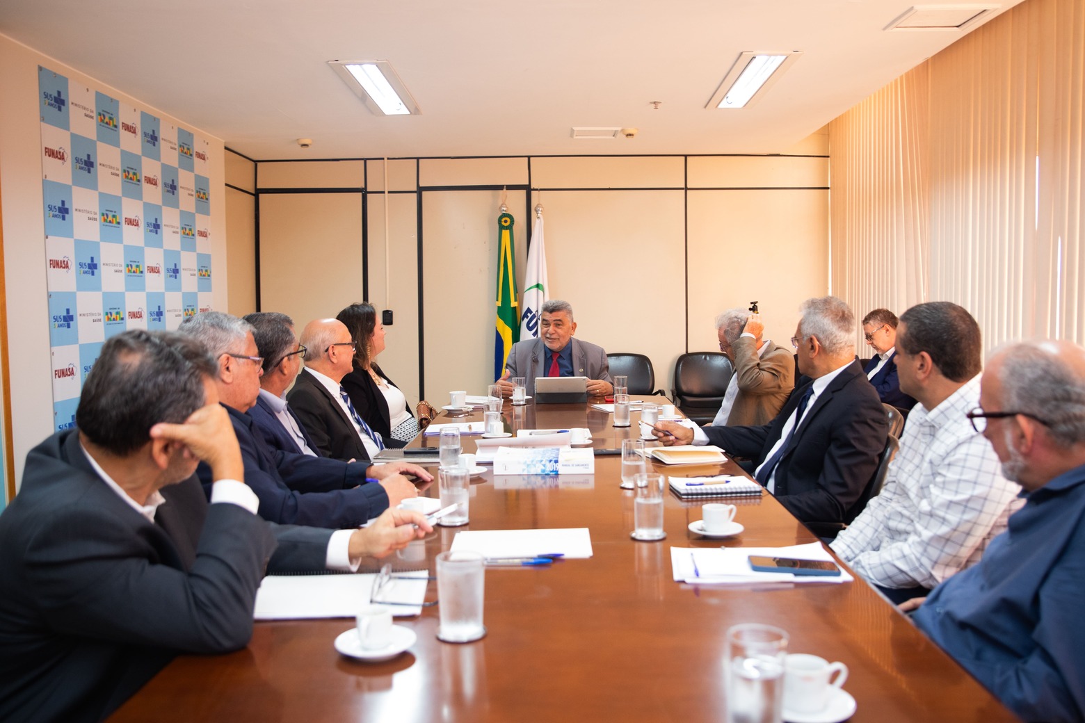 Reunião institucional com gestores e o presidente da Funasa ao centro em mesa longa.