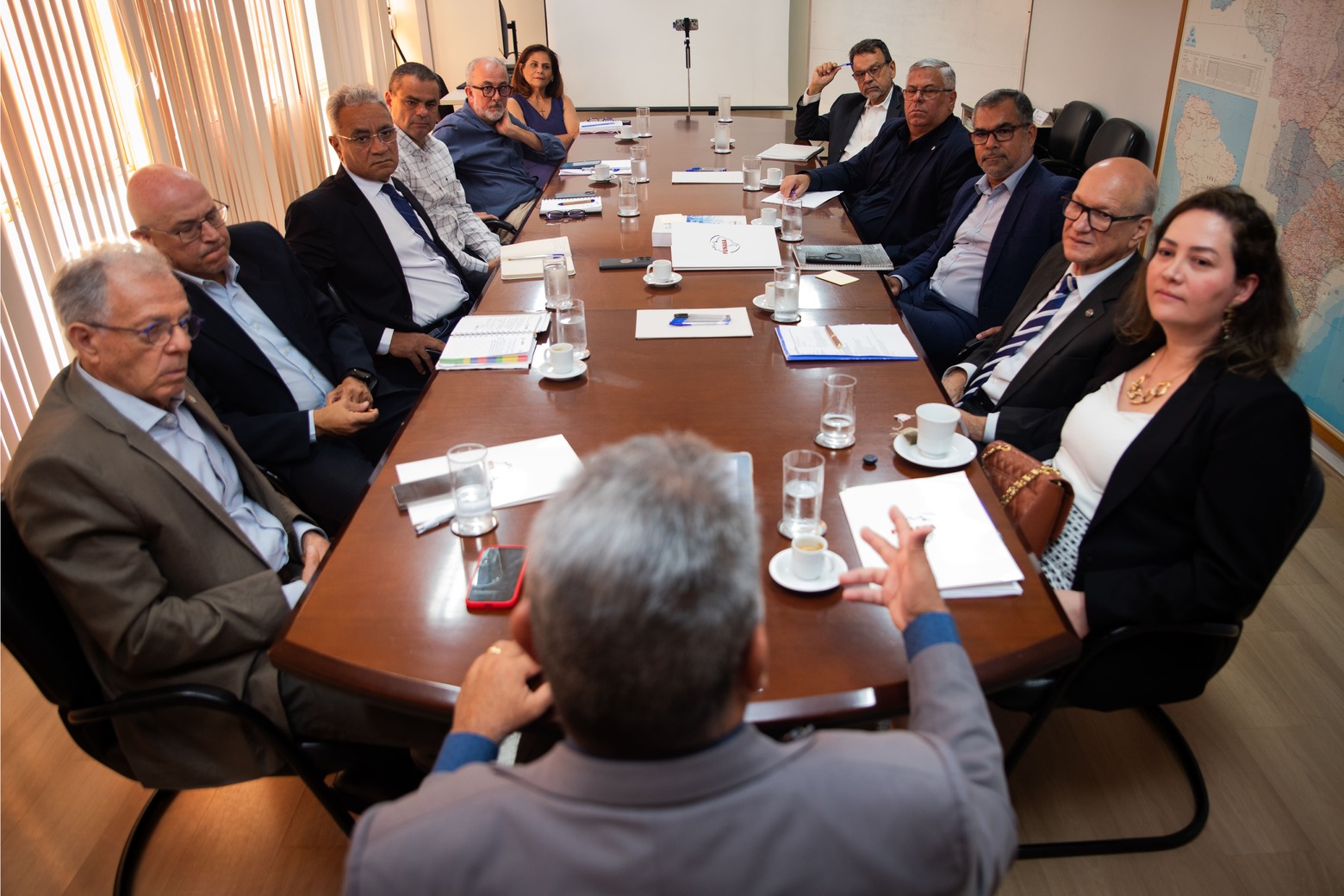 Visão de cima de reunião corporativa com equipe de perfil e o presidente ao fundo.