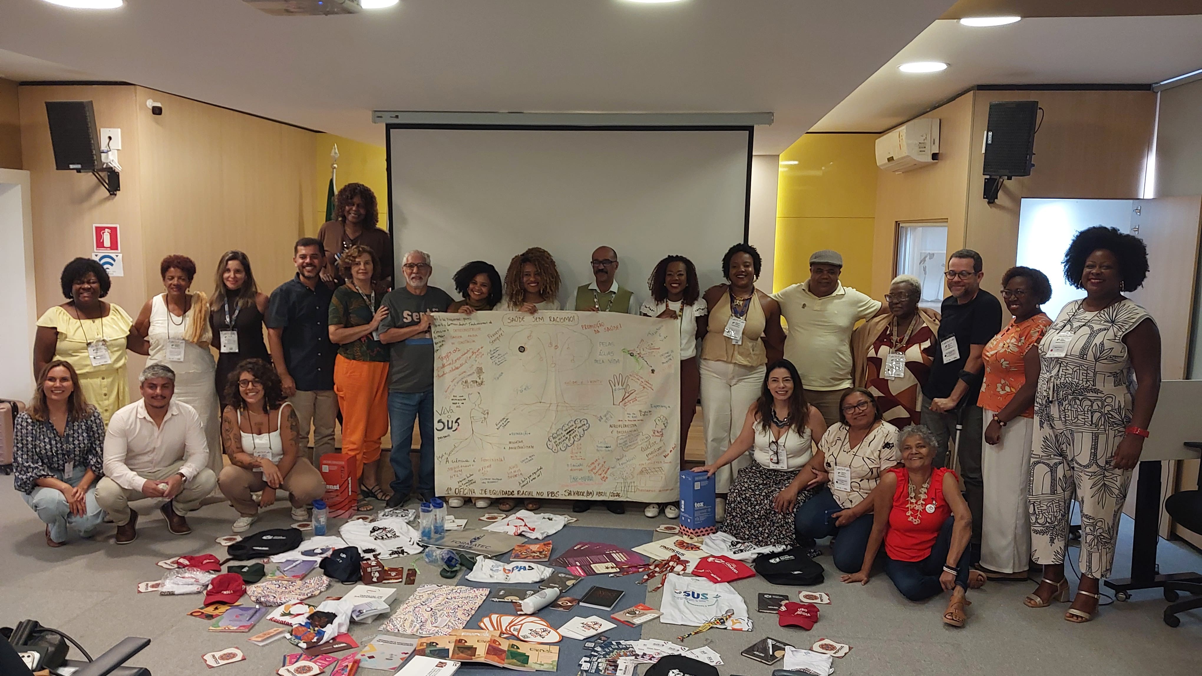 Pessoas em auditório segurando cartaz com árvore desenhada e a frase 'Saúde Sem Racismo'.