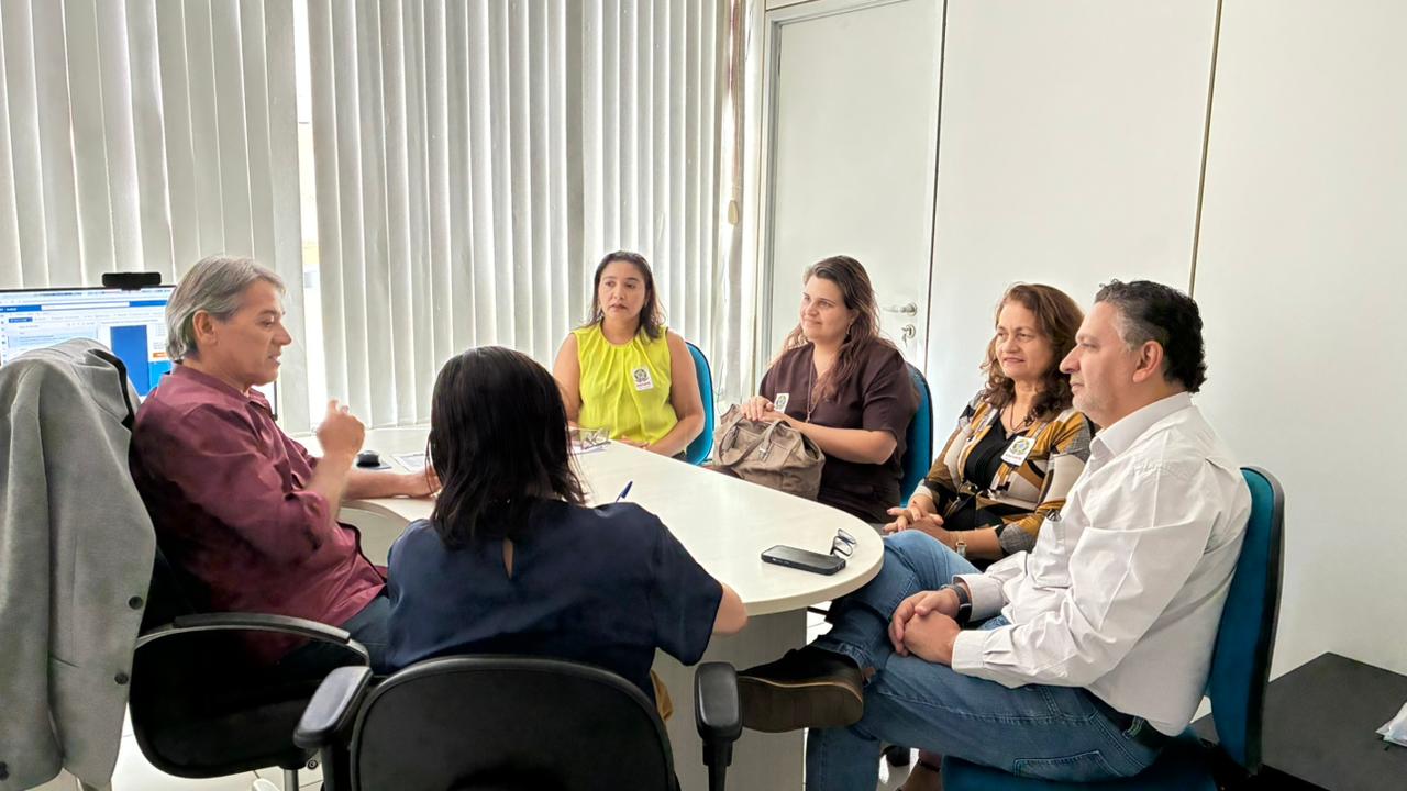 Reunião entre 6 pessoas, entre homens e mulheres, em volta de uma mesa branca.