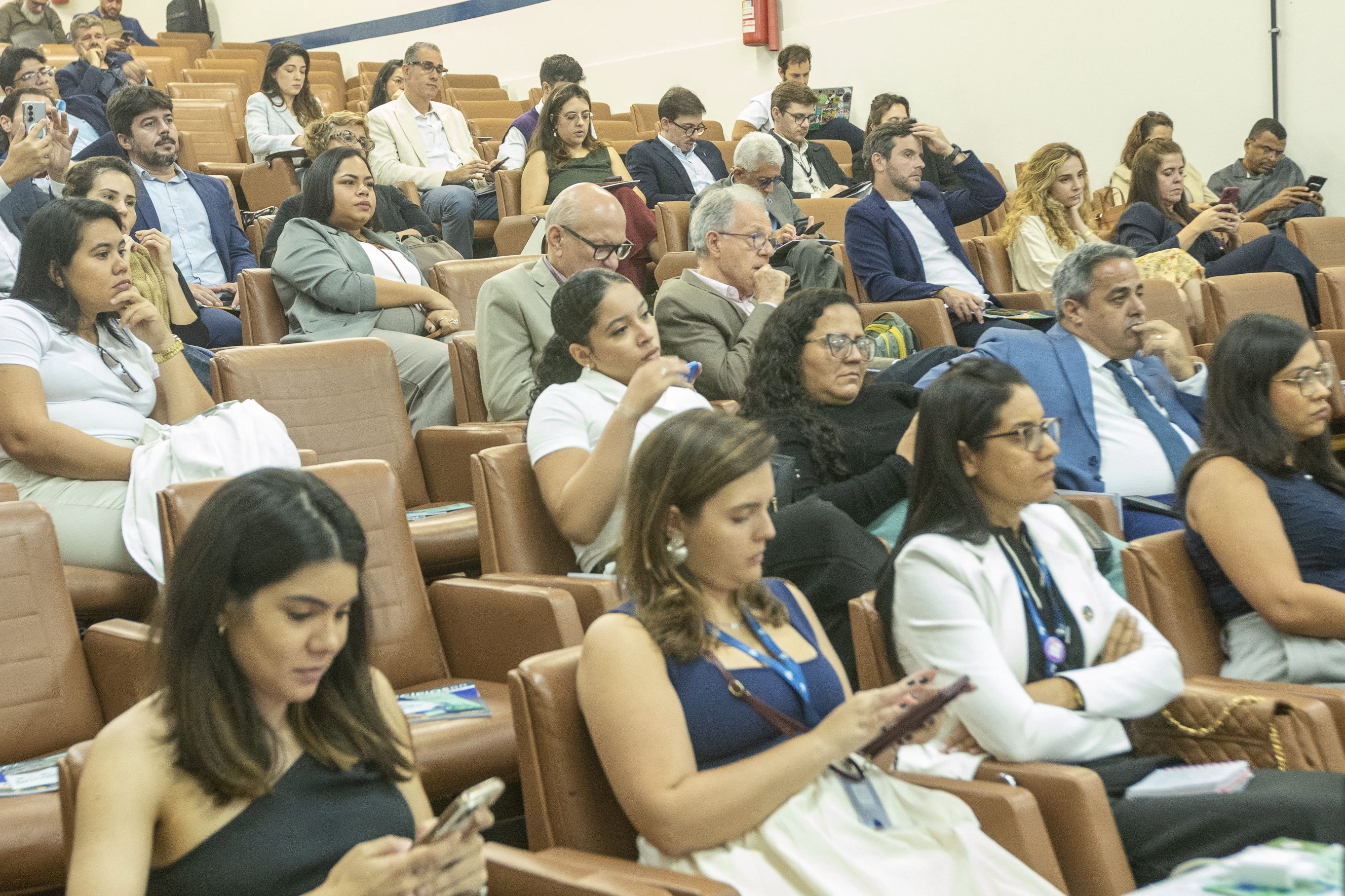 Diversas pessoas em cadeiras de um sala de palestras, ouvindo atentamente o palestrante.