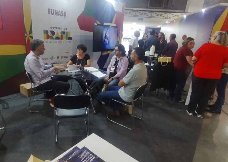 Reunião no estande da Funasa com gestores municipais, promovendo orientações sobre ações de saneamento.